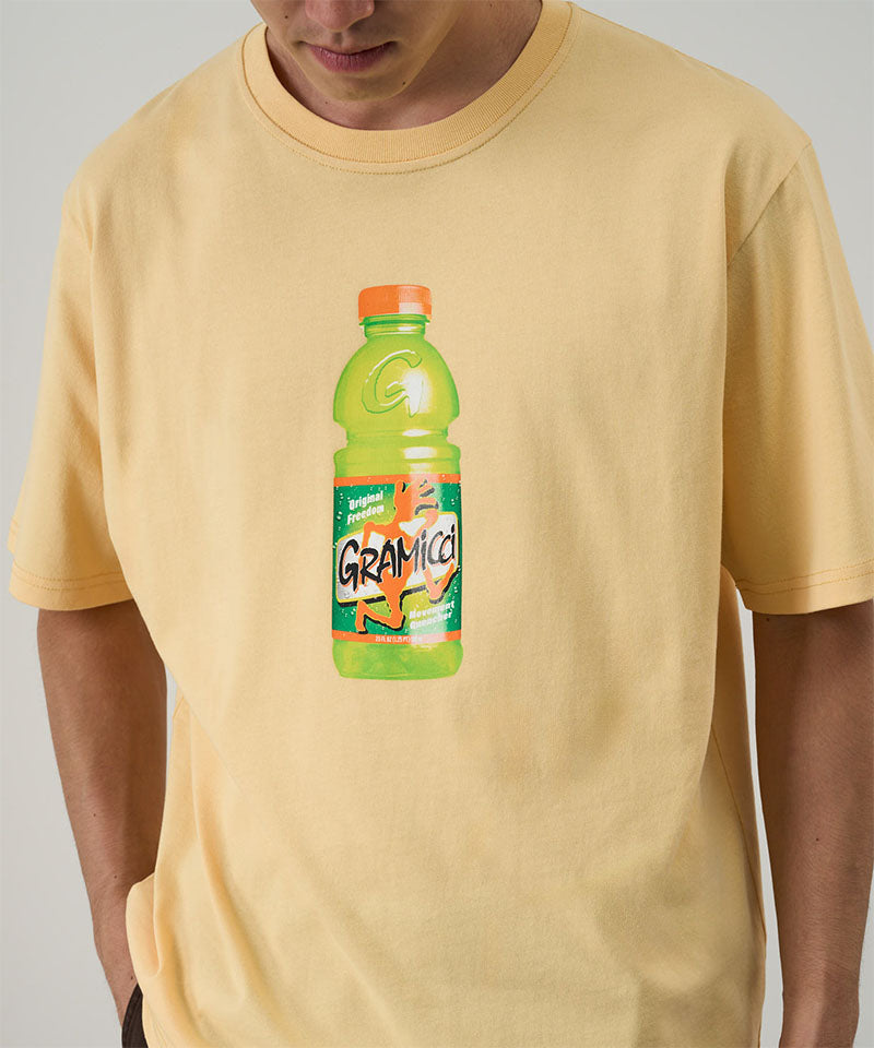 Model wearing a Gramicci mango Quencher Tee with hydration drink graphic against a light tone background.