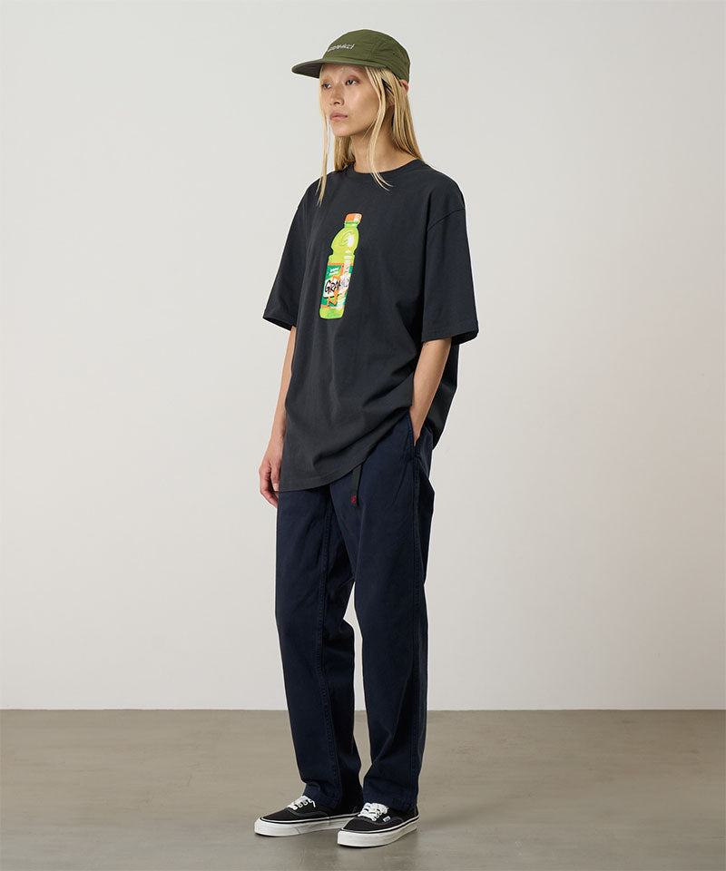 Model wearing a vintage black Gramicci Quencher Tee with a hydration drink graphic and blue pants on a light tone background.