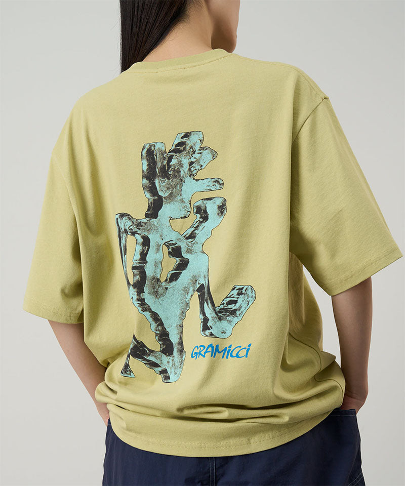 Back view of a model wearing a Gramicci lime colored Ice Sculpture Tee with a running man graphic against a light tone background.