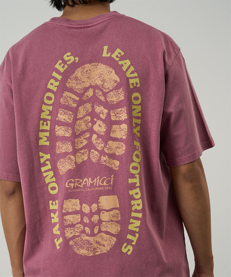 Back view of a model wearing a Gramicci red pigment Footprints Tee Pigment Dyed with yellow graphic against a light tone background.