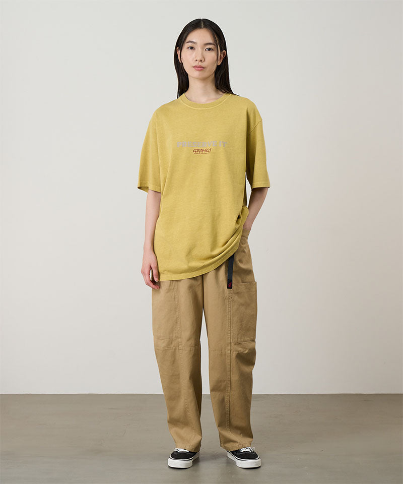 Model wearing a sulphur pigment Gramicci Footprints Tee Pigment Dyed with a grey graphic and beige pants on a light tone background.