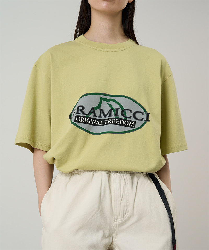 Model wearing a lime green Gramicci Half Dome Tee with a grey and green graphic and light beige pants on a light tone background.