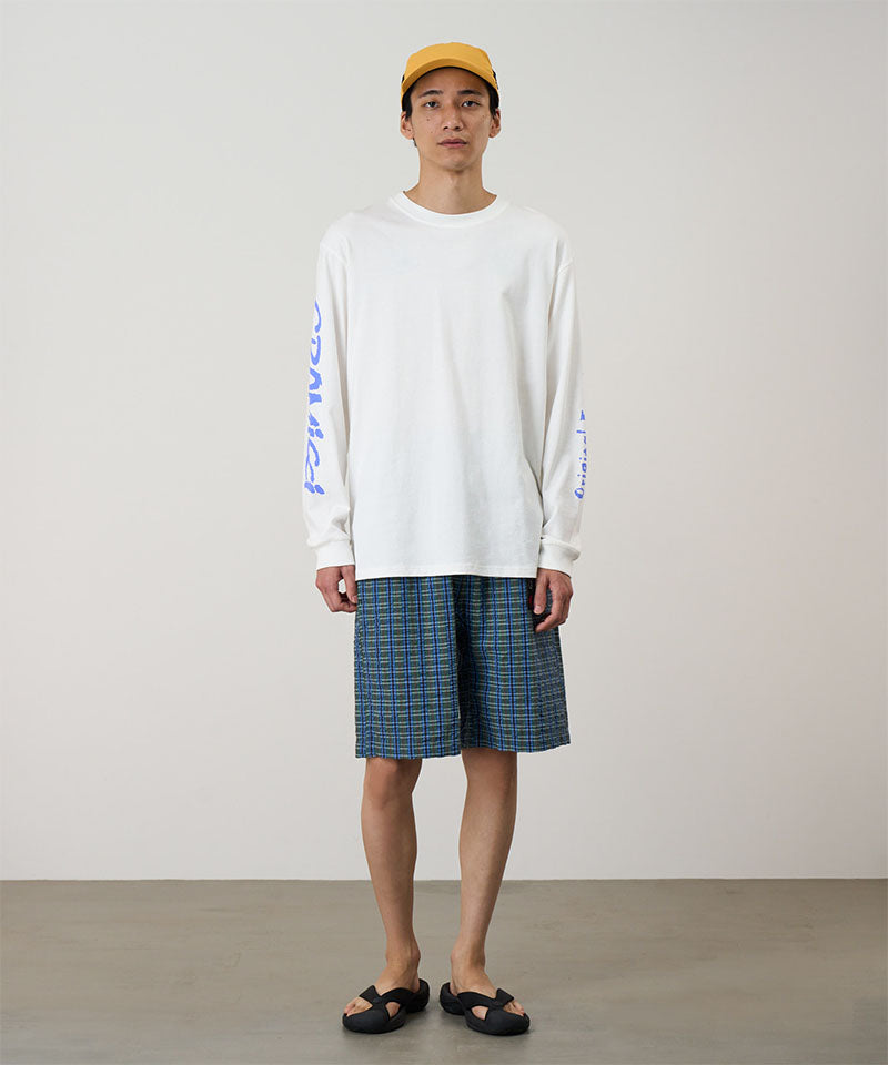 Person wearing a white long-sleeve shirt and plaid shorts standing against a plain background