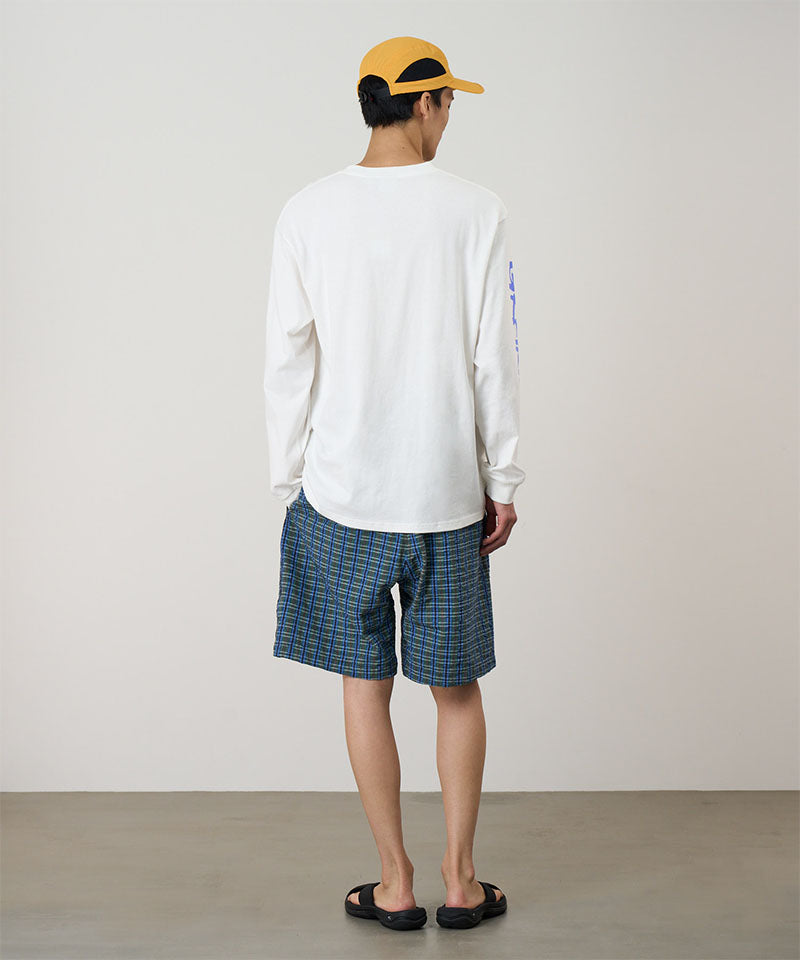 Person wearing a white long-sleeve shirt and blue plaid shorts with a yellow cap on a plain background