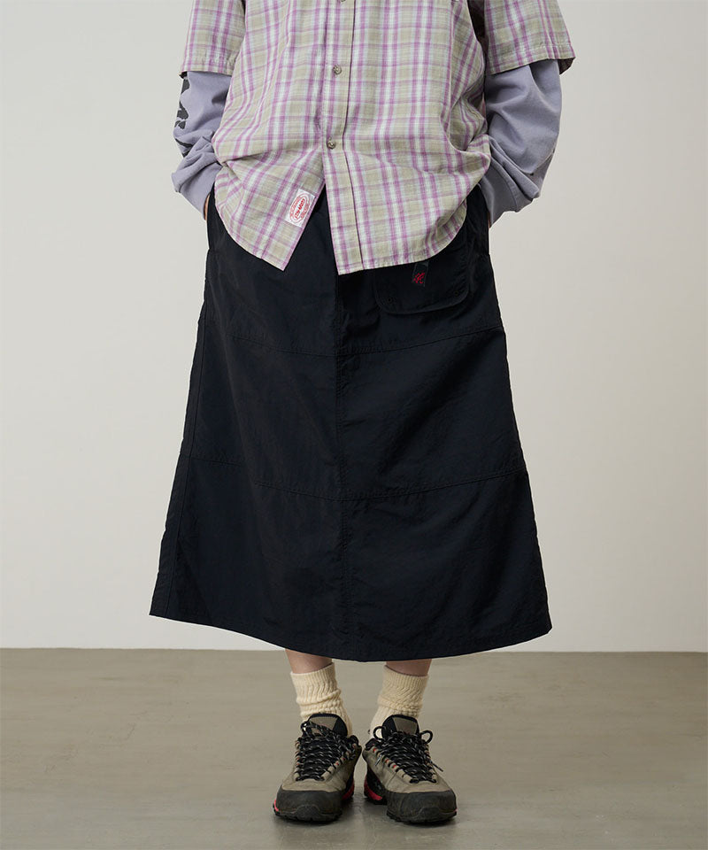 Person wearing a plaid shirt, black skirt, and hiking shoes on a plain background