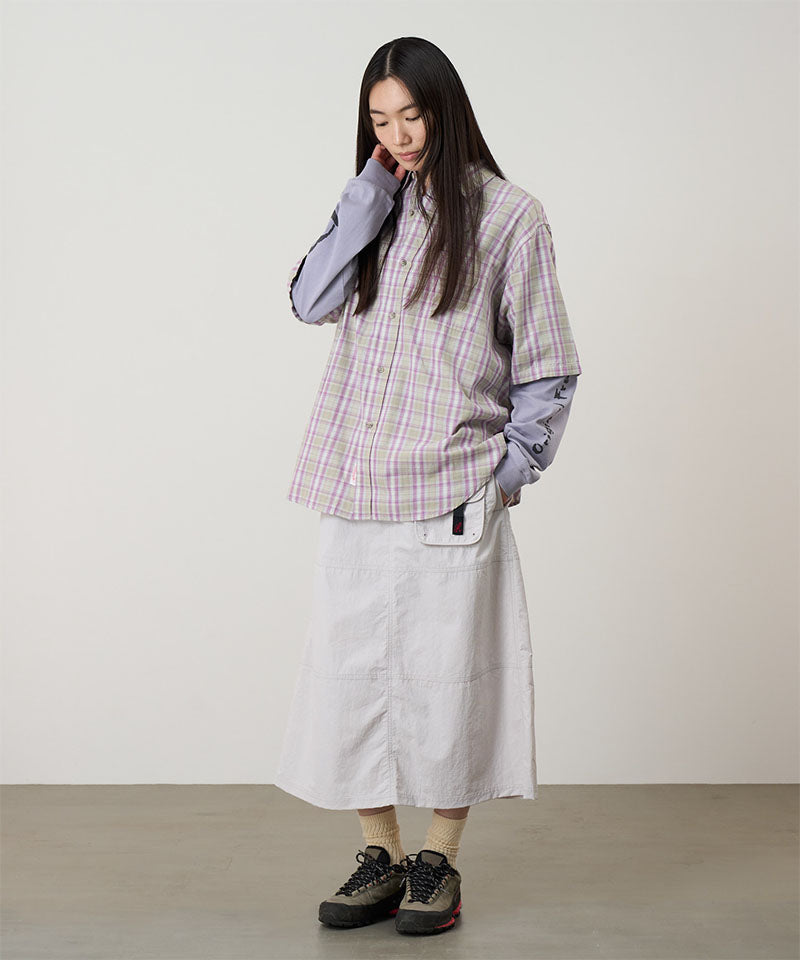 Model wearing a ecru colored Gramicci Nylon Utility Skirt and plaid shirt on a light-tone background.