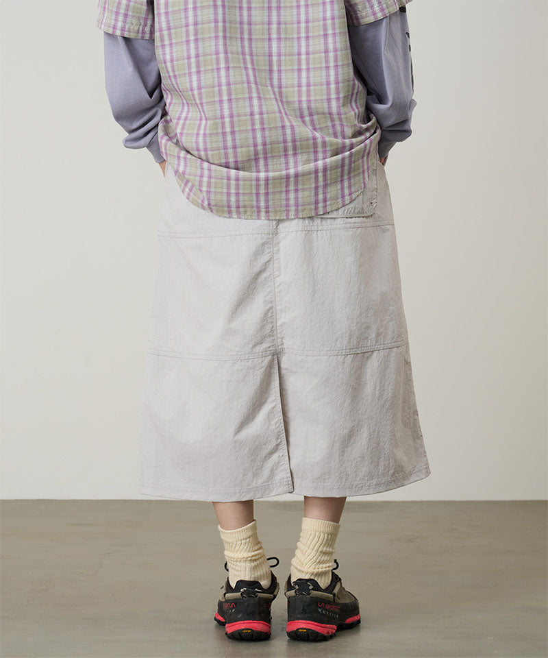 Person wearing a plaid shirt, light gray skirt, and black shoes on a plain background