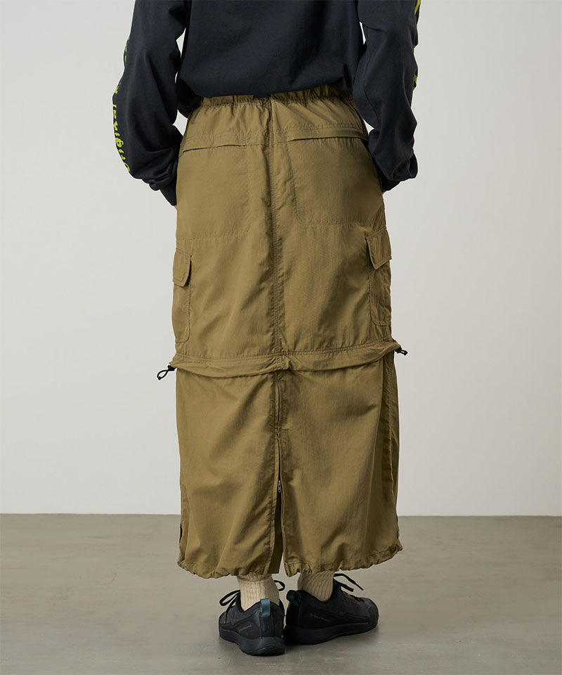 Back view of a model wearing a Gramicci Convertible Cargo Skirt in the color khaki and a black shirt on a light-tone background.