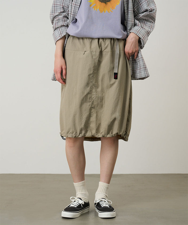 Person wearing a plaid shirt, gray top with sunflower design, beige skirt, and black sneakers on a plain background