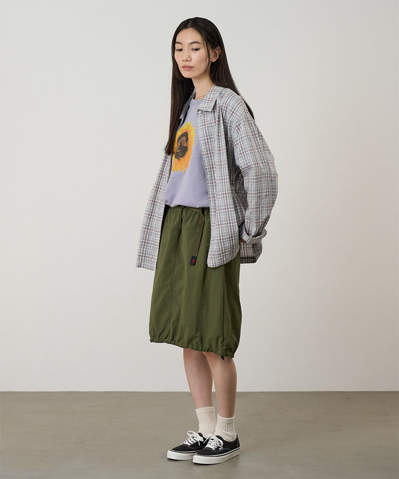 Person wearing a plaid shirt over a graphic t-shirt with a green skirt on a plain background