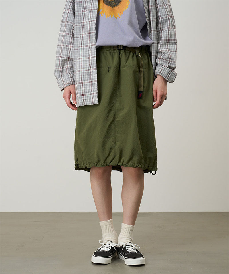 Person wearing a green skirt, plaid shirt, and black sneakers on a plain background