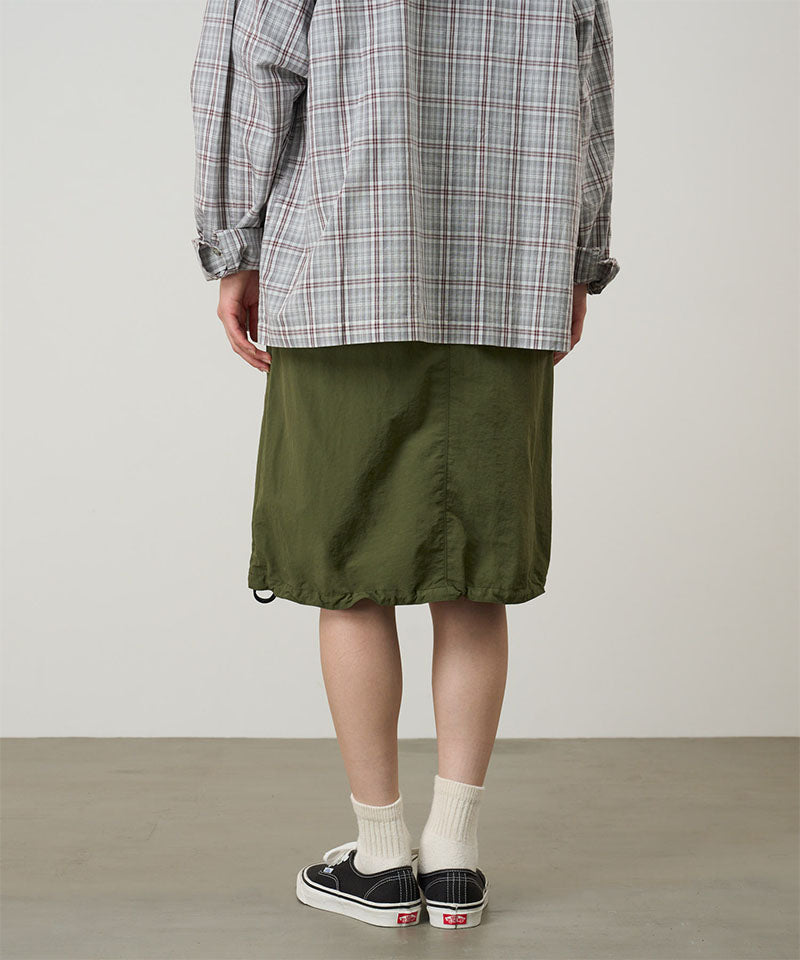 Person wearing a plaid shirt, green skirt, and black sneakers on a plain background