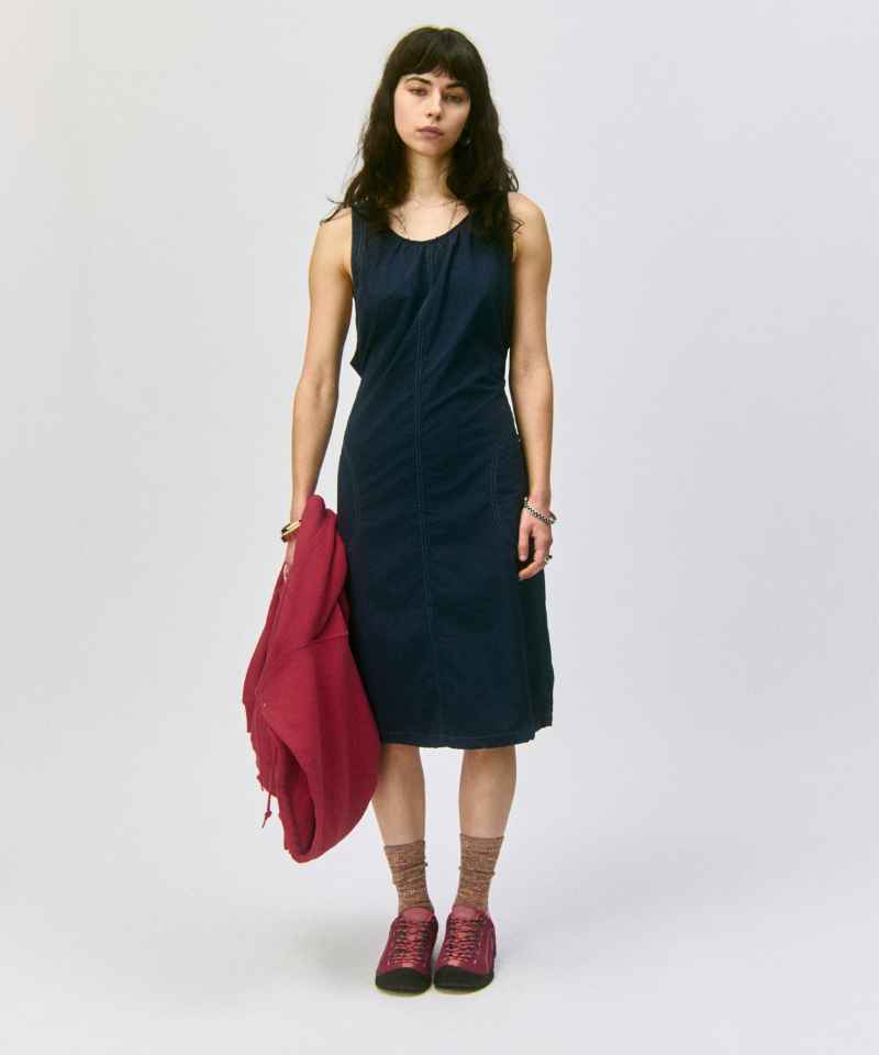 Model wearing a navy dress holding a red jacket and Gramicci Hemp Blend Socks on a light-tone background.