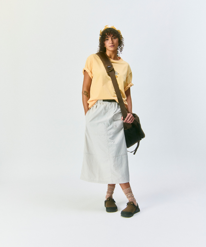 Model wearing a mango colored t-shirt, light gray skirt, amber Hemp Blend Socks, and brown shoes on a light-tone background.