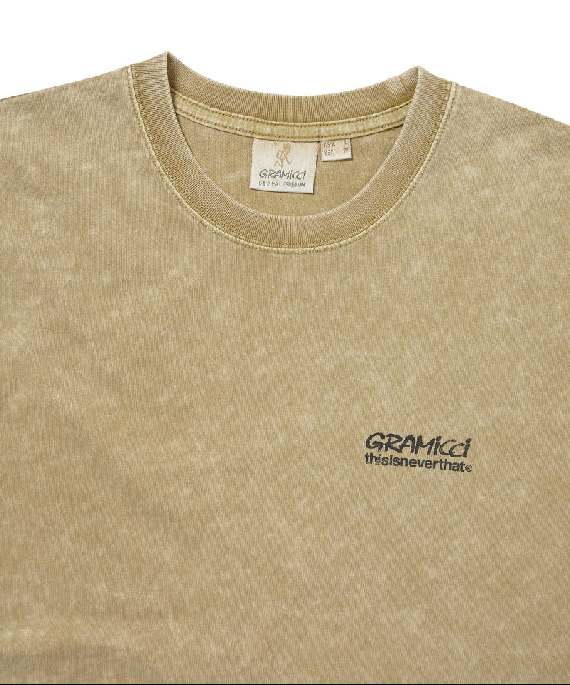 Close-up of a beige mineral-wash t-shirt with a small black embroidered logo on the left chest reading 'GRAMICCI thisisneverthat'.