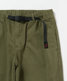 Close-up of olive green pants with a black belt featuring a small red embroidered Gramicci logo.