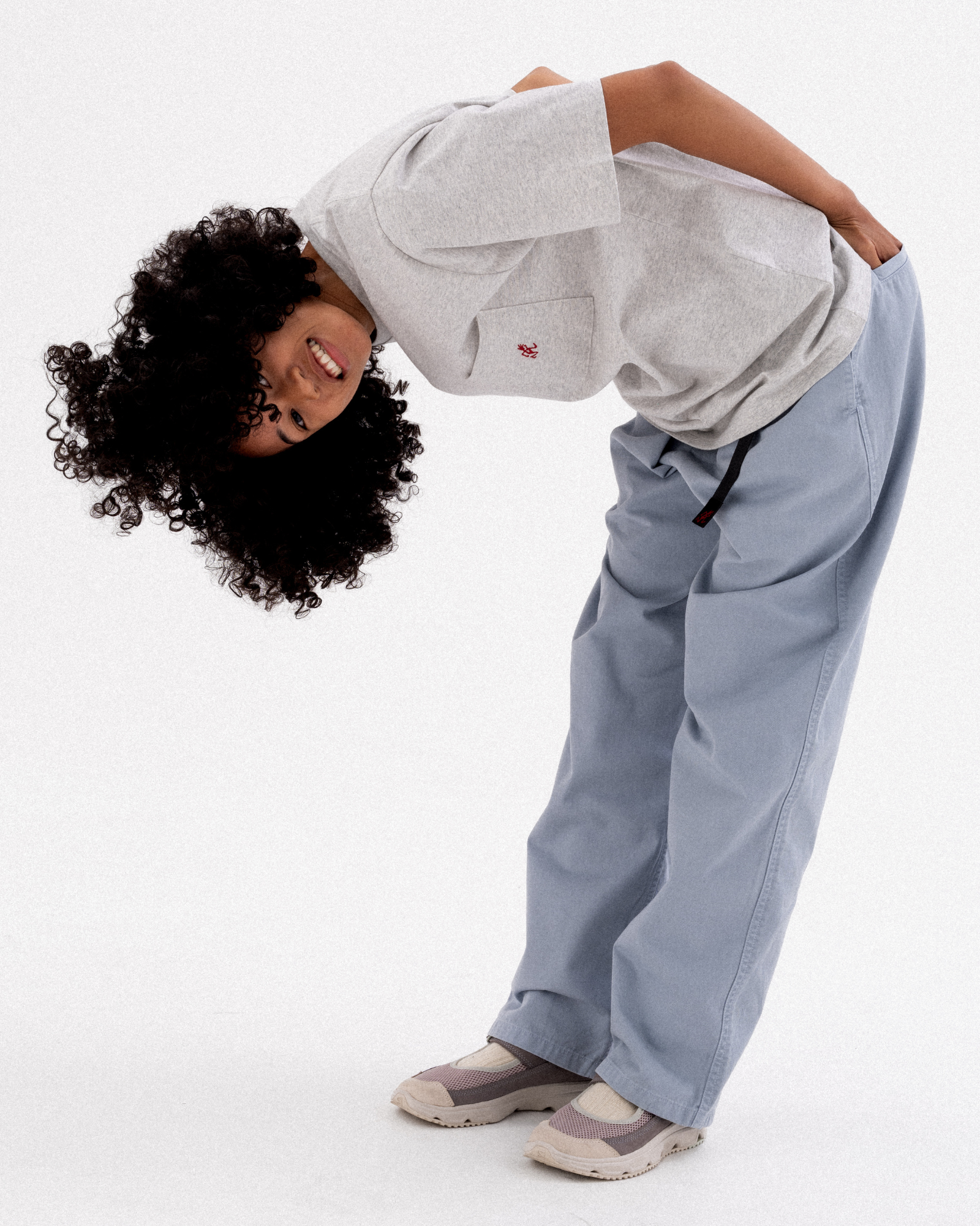 A model wearing a light gray heather crewneck sweatshirt and light blue wide-leg pants, leaning forward on a white studio background.
