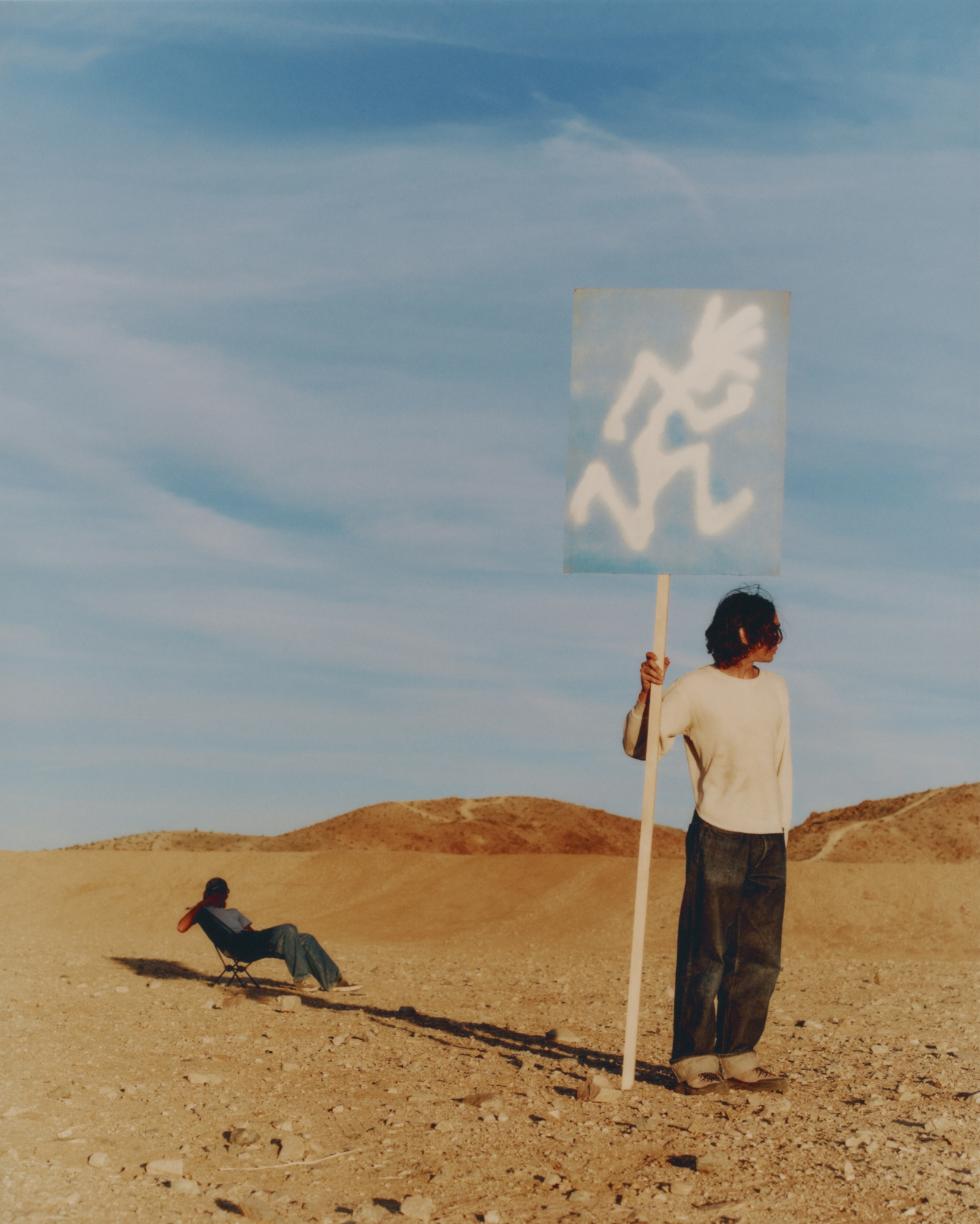 Person holding a sign with a white Gramicci symbol in a desert landscape