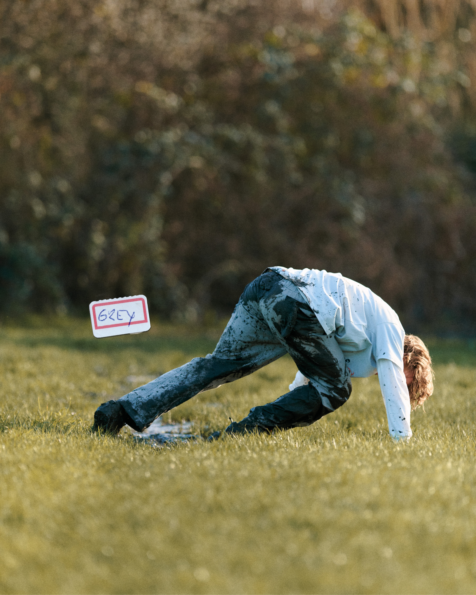 Person in a muddy field with a sign labeled 'GREY' in the foreground