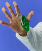 Hand holding a key with a green Gramicci Hotel Keychain against a blue background