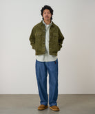 Model wearing blue Japanese Chambray Rock Slide Pant and a moss green jacket on a light-tone background.