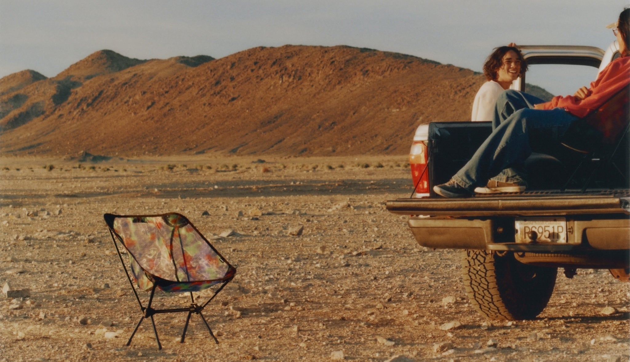 Two people sitting in the back of a pickup truck in a desert setting with a Gramicci & Helinox Chair One.