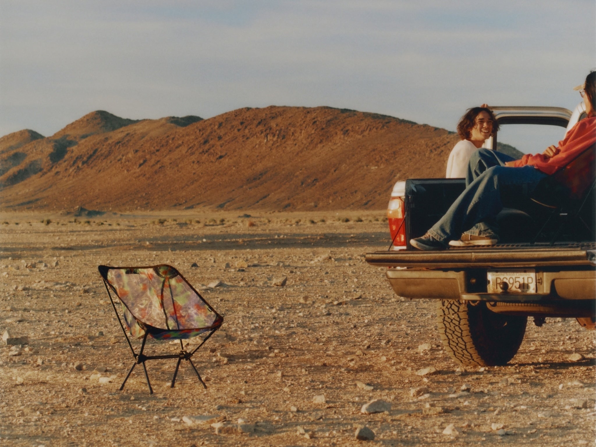 Two people sitting in the back of a pickup truck in a desert setting with a Gramicci & Helinox Chair One.