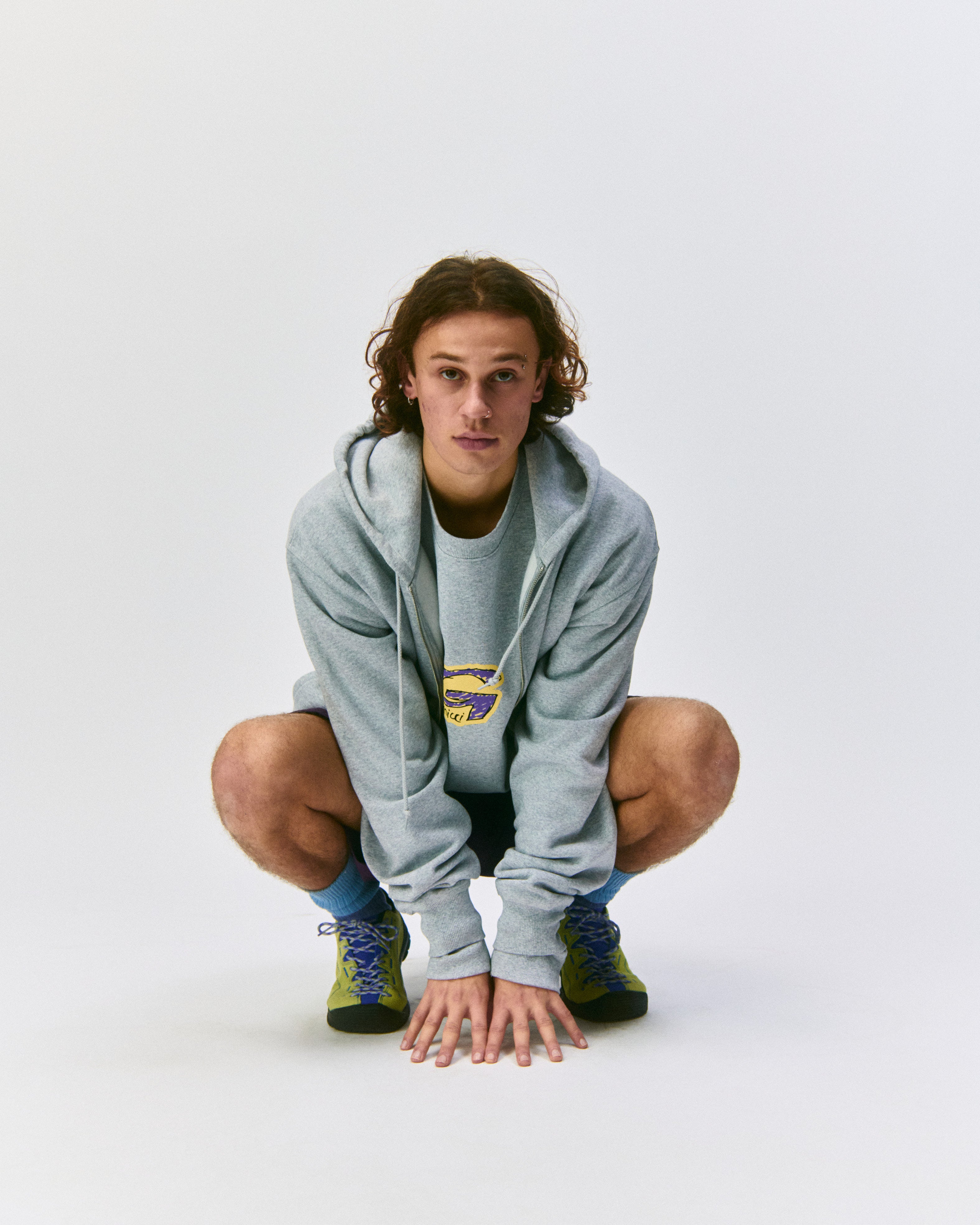 Person sitting wearing a gray hoodie with a Gramicci logo on a light-tone background.