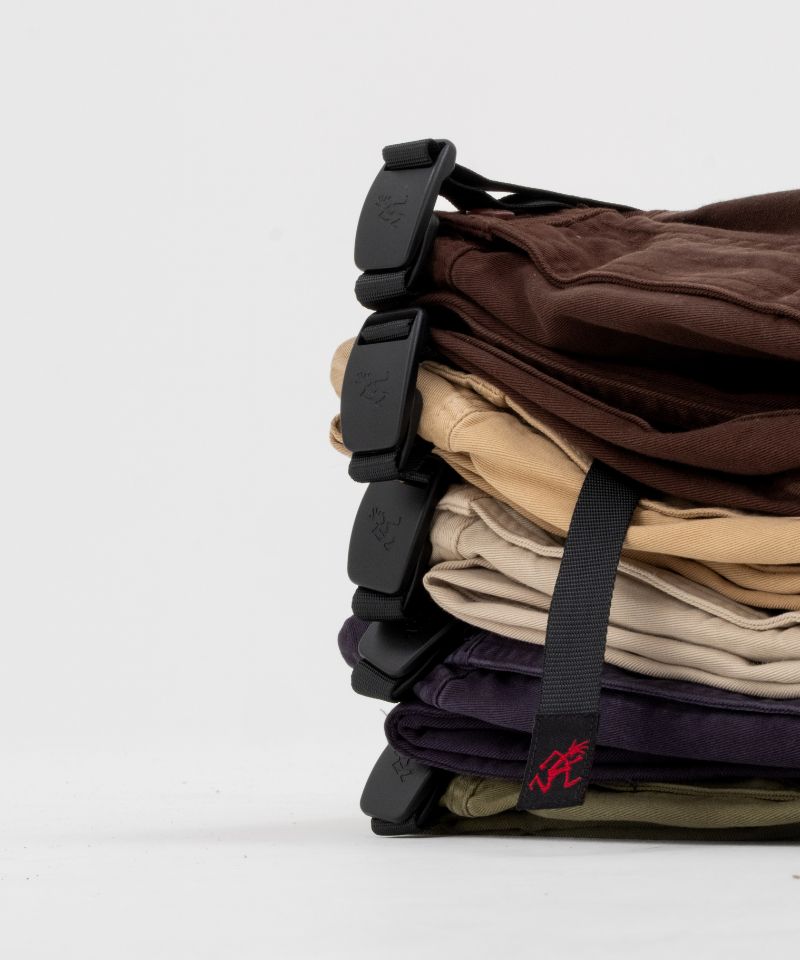 Stack of folded Gramicci Gadget Pants in various colors with a black belt on a white background