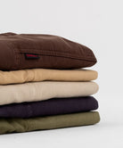 Several folded Gramicci Gadget Pants in various colors with a black belt on a white background