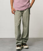 Model wearing dried sage colored Gramicci Pants and a dusty pink shirt on a light-tone background.