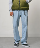 Model wearing dusty blue pigment Gramicci Pants and a olive vest on a light-tone background.