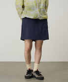 Model wearing a Gramicci G-Skort in the color double navy and a yellow patterned jacket on a light-tone background.