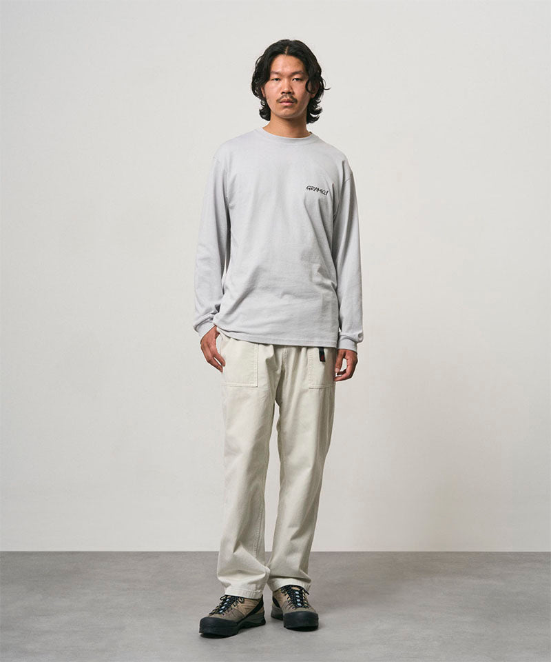 Model wearing a mist colored Gramicci Bass Long-Sleeve Tee and off-white pants on a light-tone background.