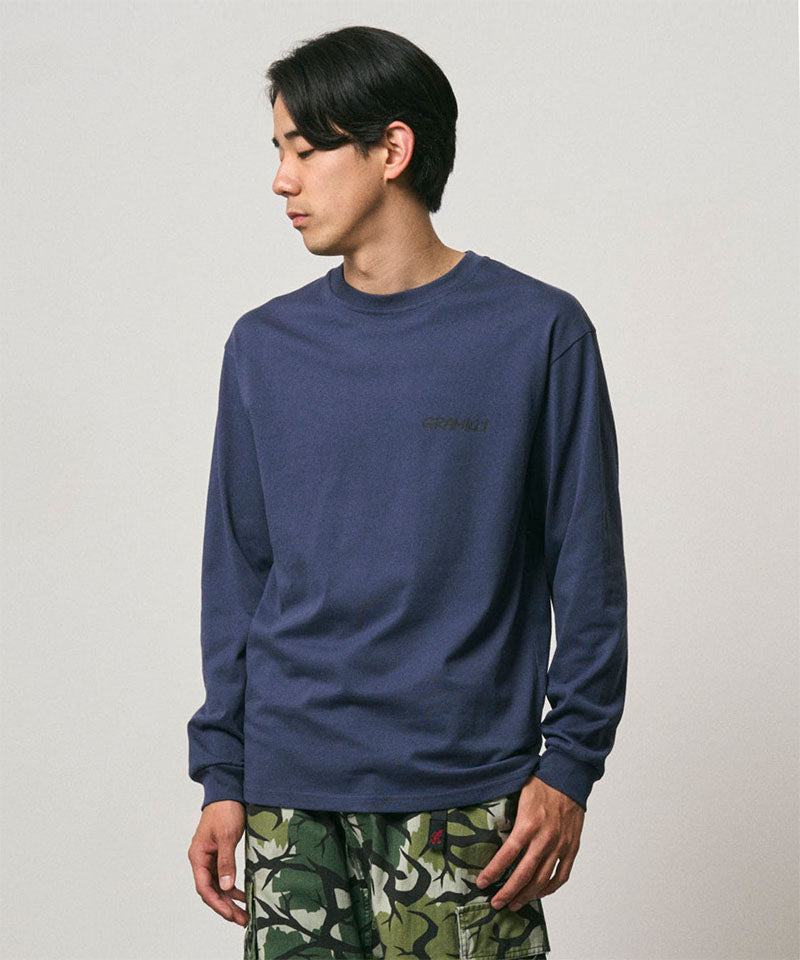Model wearing a Gramicci navy Bass Long-Sleeve Tee with a graphic against a light-tone background.