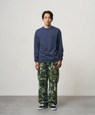 Model wearing a navy Gramicci Bass Long-Sleeve Tee and camo pants on a light-tone background.