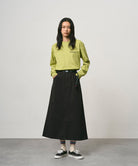 Model wearing a sweet pea colored Gramicci Bass Long-Sleeve Tee and black skirt on a light-tone background.
