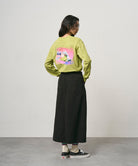 Back view of a model wearing a sweet pea colored Gramicci Bass Long-Sleeve Tee with a graphic and black skirt on a light-tone background.