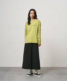 Model wearing a sweet pea colored Gramicci Bass Long-Sleeve Tee and black skirt on a light-tone background.