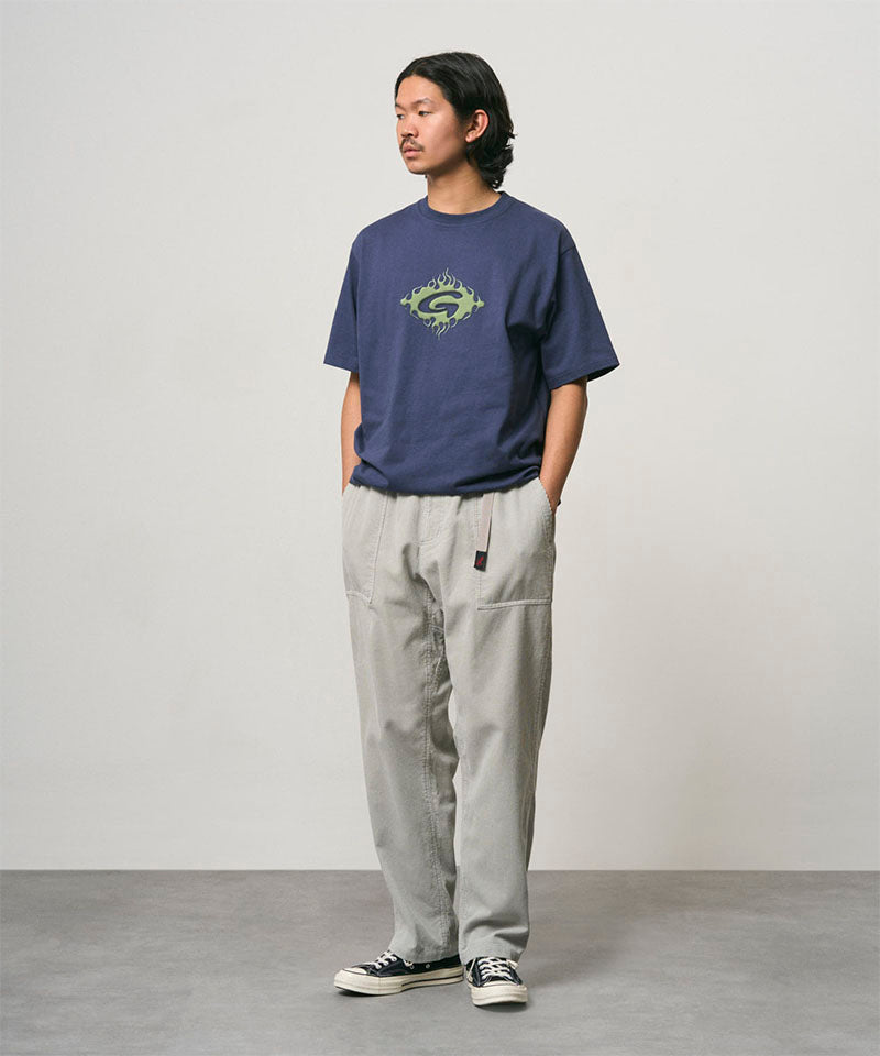Model wearing a navy Gramicci Flames Tee with a graphic and light grey pants on a light-tone background.