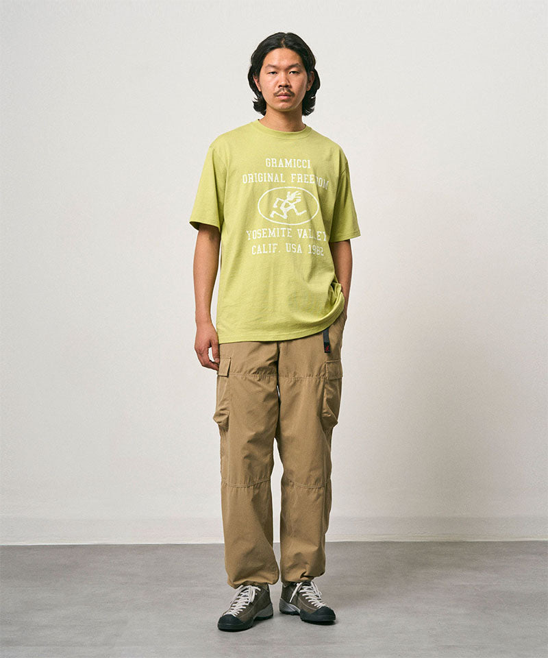 Model wearing a sweet pea colored Gramicci Flames Tee with a graphic and beige pants on a light-tone background.
