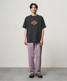Model wearing a vintage black Gramicci Flames Tee with a graphic and lavender pants on a light-tone background.