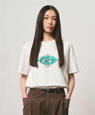 Model wearing a Gramicci white Flames Tee with a graphic against a light-tone background.