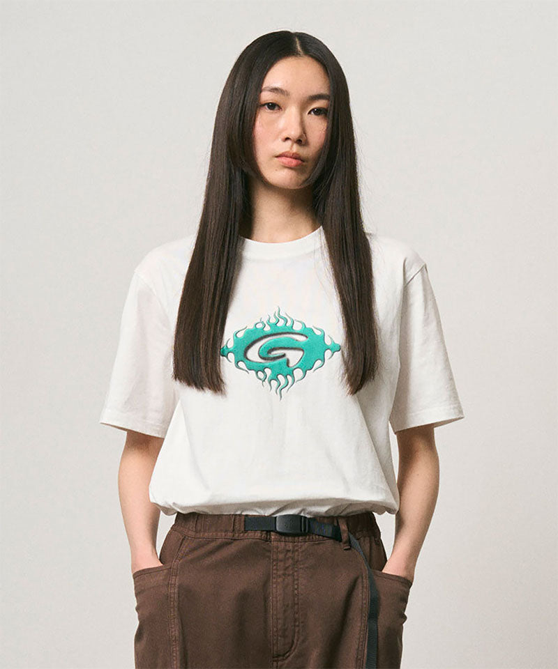 Model wearing a Gramicci white Flames Tee with a graphic against a light-tone background.