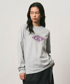 Model wearing a Gramicci mist colored Flames Long Sleeve Tee with a graphic against a light-tone background.