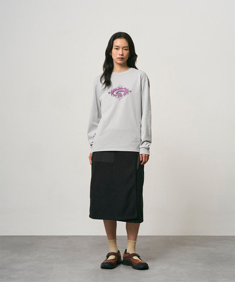 Model wearing a mist colored Gramicci Flames Long Sleeve Tee with a graphic and black skirt on a light-tone background.