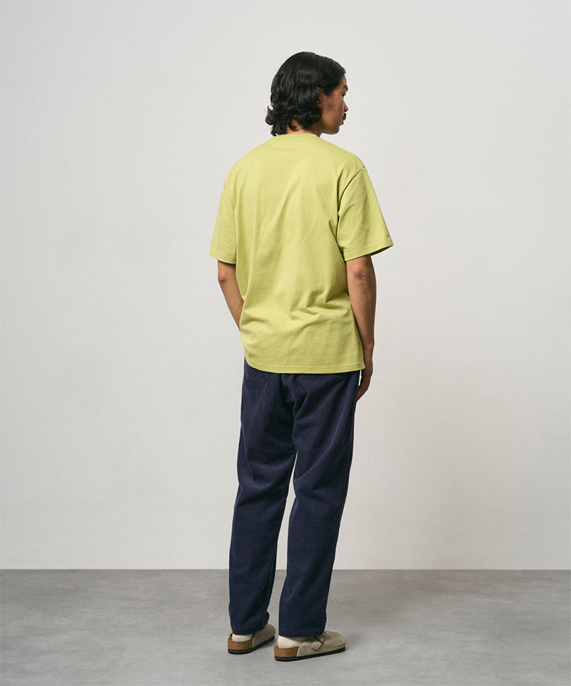 Back view of a model wearing a sweet pea colored Gramicci Ladybug Tee and blue pants on a light-tone background.