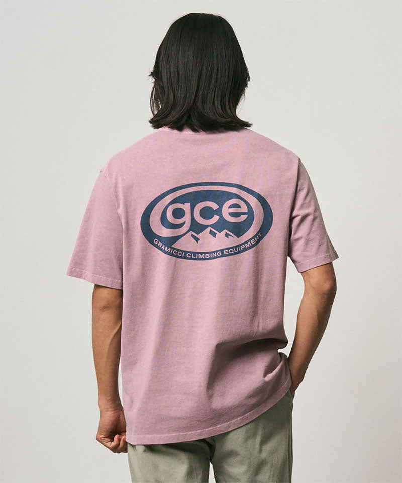 Model wearing a Gramicci lilac pigment colored GCE Tee Pigment Dyed with a graphic against a light-tone background.
