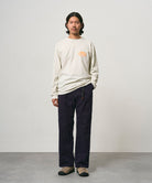 Model wearing a natural pigment colored Gramicci GCE Tee Pigment Dyed and black pants on a light-tone background.