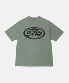 Back view of a Gramicci sage pigment colored GCE Tee Pigment Dyed with a graphic against a light-tone background.